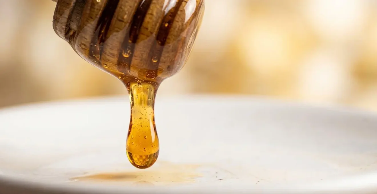 Dettaglio macro della texture cremosa del miele italiano su superficie naturale