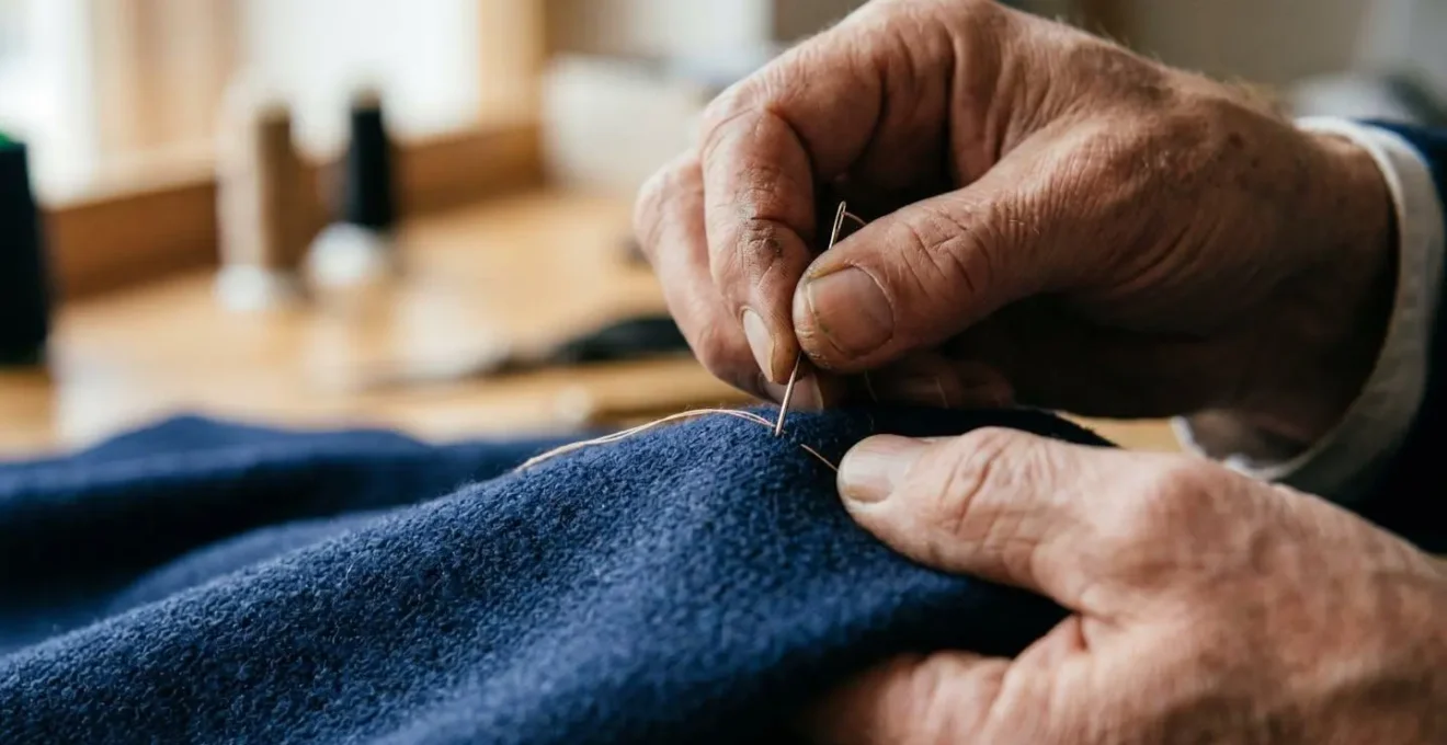 Mani esperte di un artigiano sarto italiano che lavorano su una cucitura a mano con ago e filo, dettaglio macro