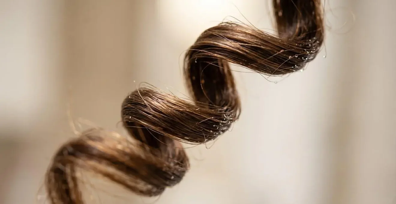 Dettaglio macro di ciocca di capelli ricci durante asciugatura con diffusore che mostra la formazione del boccolo